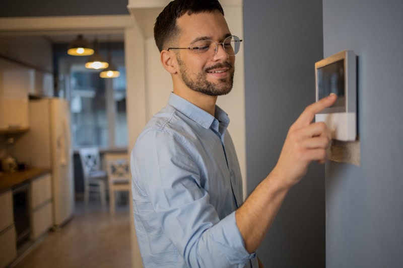 Young man adjusts the temperature at home with a device on the wall.